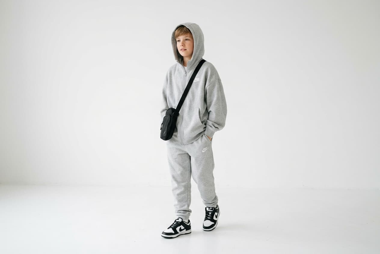 a young english 10-year old hooded teen boy with trim hair loitering with hands tucked into pockets dressed with crossbag close beside, over flowing, Wind tousled light grey hooded oversized zip up track suit with hood on, small white nike logo over joggers with white nike logo over nike dunk trainers in a white studio. a young english 10-year old hooded teen boy with trim hair loitering with hands tucked into pockets dressed with crossbag close beside, over flowing, Wind tousled light grey hooded oversized zip up track suit with hood on, small white nike logo over joggers with white nike logo over nike dunk trainers in a white studio. CVY.AI