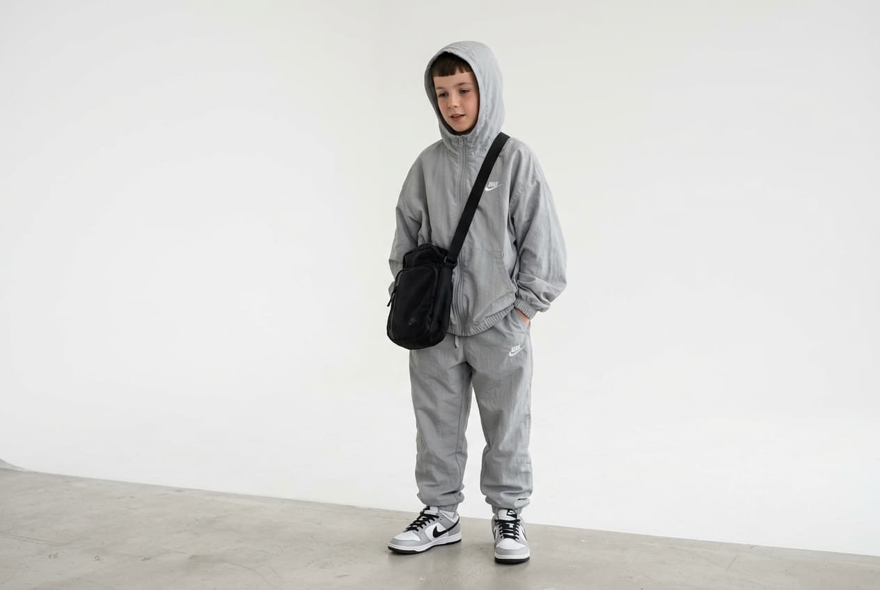 a young english 10-year old hooded teen boy with trim hair loitering with hands tucked into pockets dressed with crossbag close beside, over flowing, Wind tousled light grey hooded oversized zip up track suit with hood on, small white nike logo over joggers with white nike logo over nike dunk trainers in a white studio. a young english 10-year old hooded teen boy with trim hair loitering with hands tucked into pockets dressed with crossbag close beside, over flowing, Wind tousled light grey hooded oversized zip up track suit with hood on, small white nike logo over joggers with white nike logo over nike dunk trainers in a white studio. CVY.AI